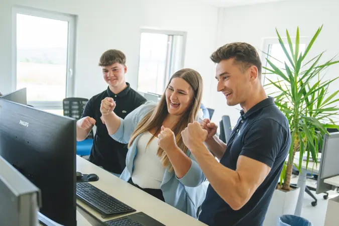 People in front of desk with computer, celebrating a success.