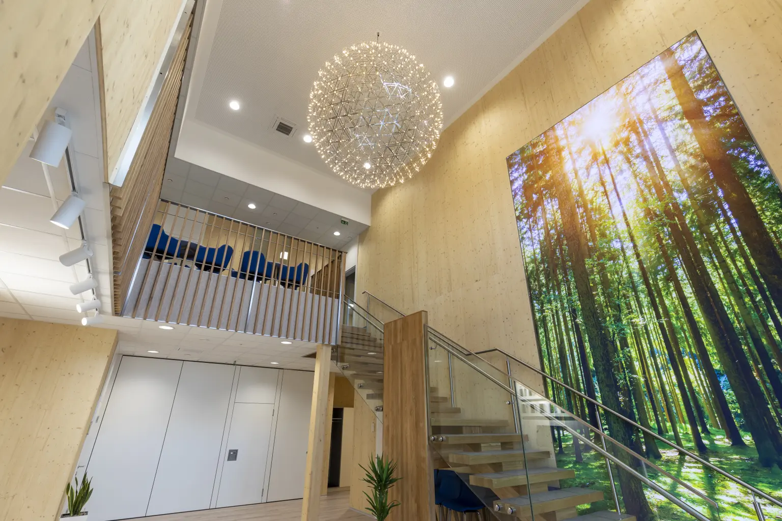 Foyer with large lampshade resembling the sun, wooden walls, glass stair railing, and huge forest picture on the wall.