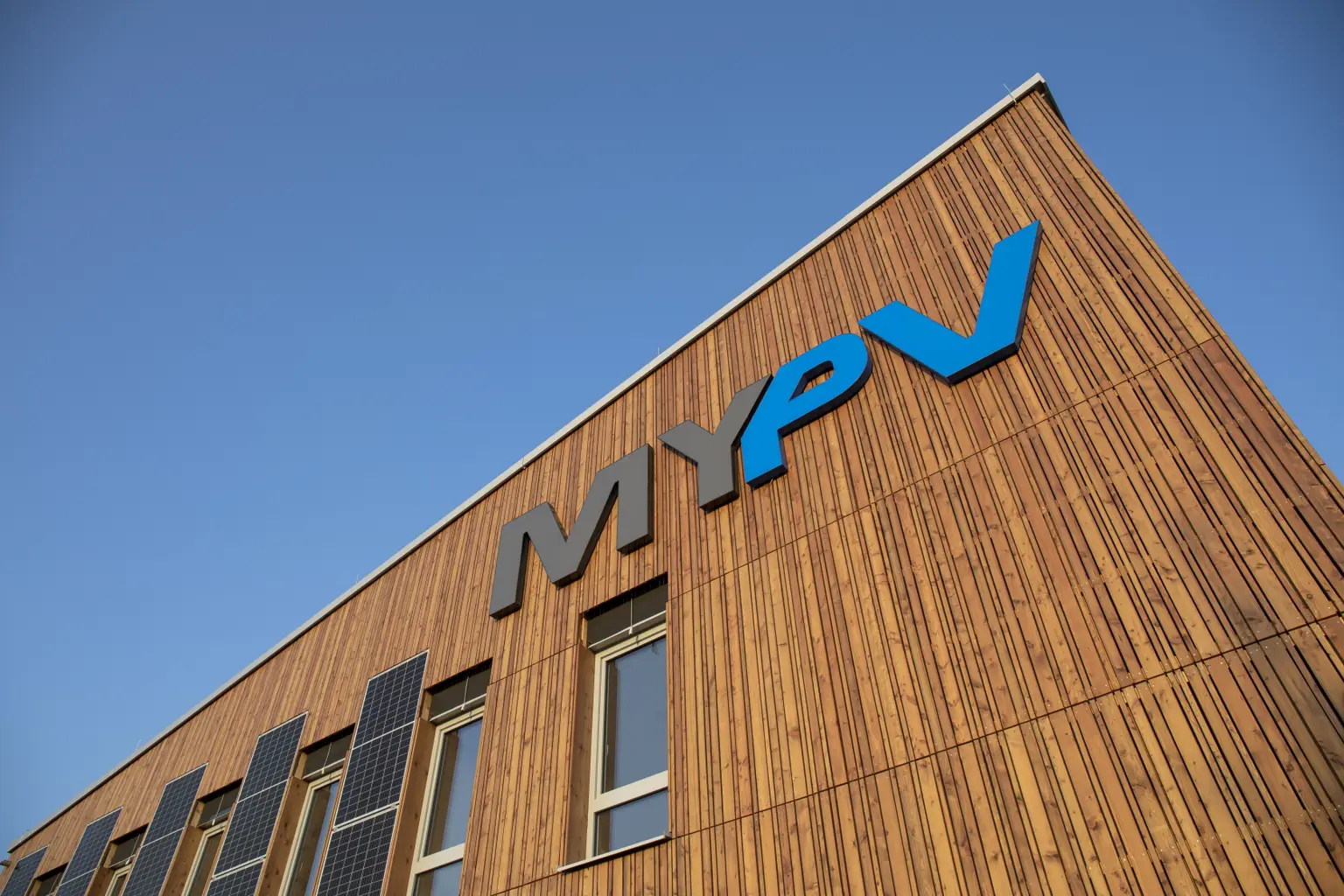 Photo of company building taken from below, showing logo on the wall and several photovoltaic panels on the roof.