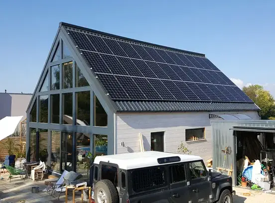 Modern house with large windows and solar panels on roof, white SUV parked in front under clear blue sky
