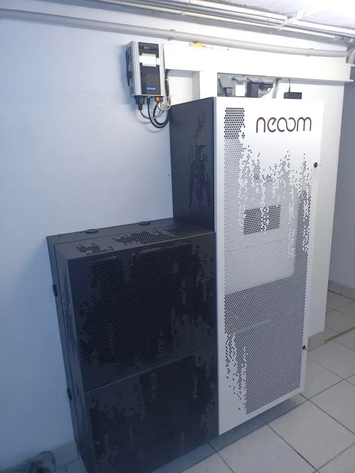 Large heat storage unit with white and black exterior, 'necom' logo, installed in a room with tiled floor.