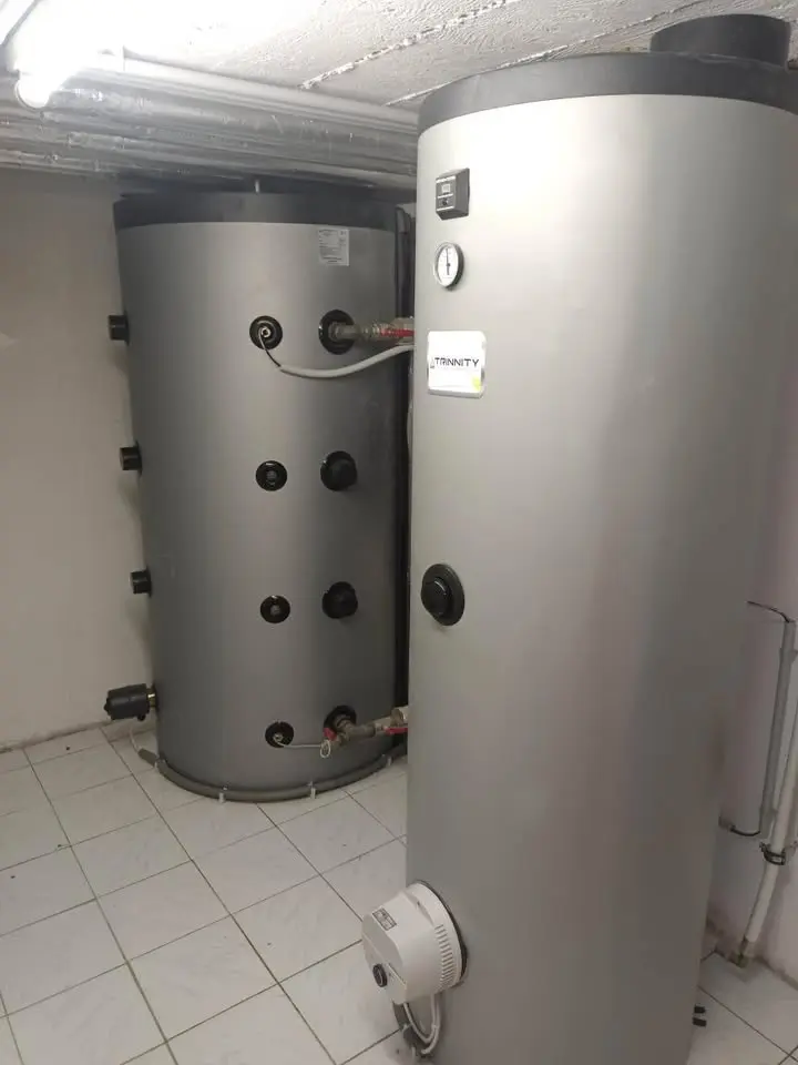 Two large gray cylindrical water heaters in a tiled basement room, with visible pipes and gauges.