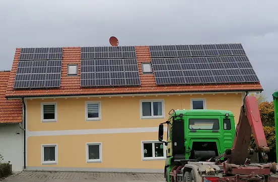 House with orange roof, solar panels, yellow walls, white trim, and a green truck parked in front under an overcast sky.