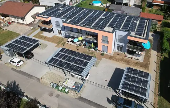 Multi-family house with rooftop PV panels; parking area in front has carports with PV panels on their roofs.