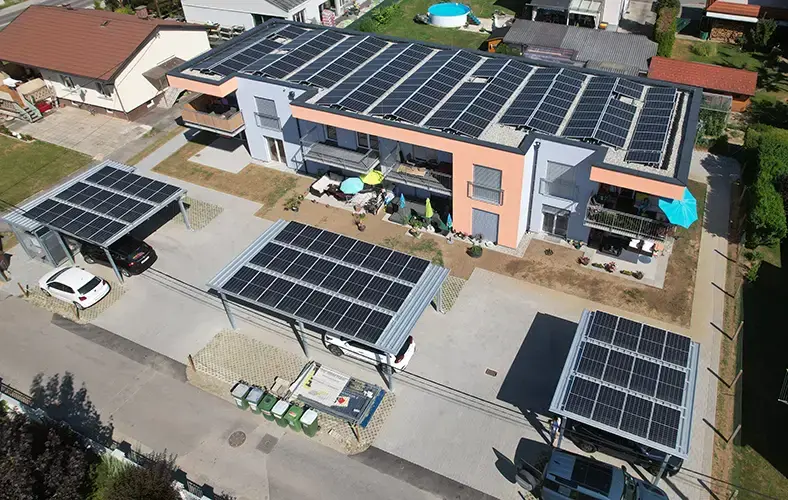 Multi-family house with rooftop PV panels; parking area in front has carports with PV panels on their roofs.