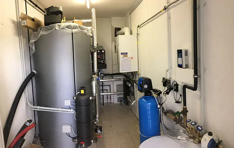 Utility room with large gray water heater, pipes, blue pressure tank, control panels, and a connected AC•THOR 9s on the walls