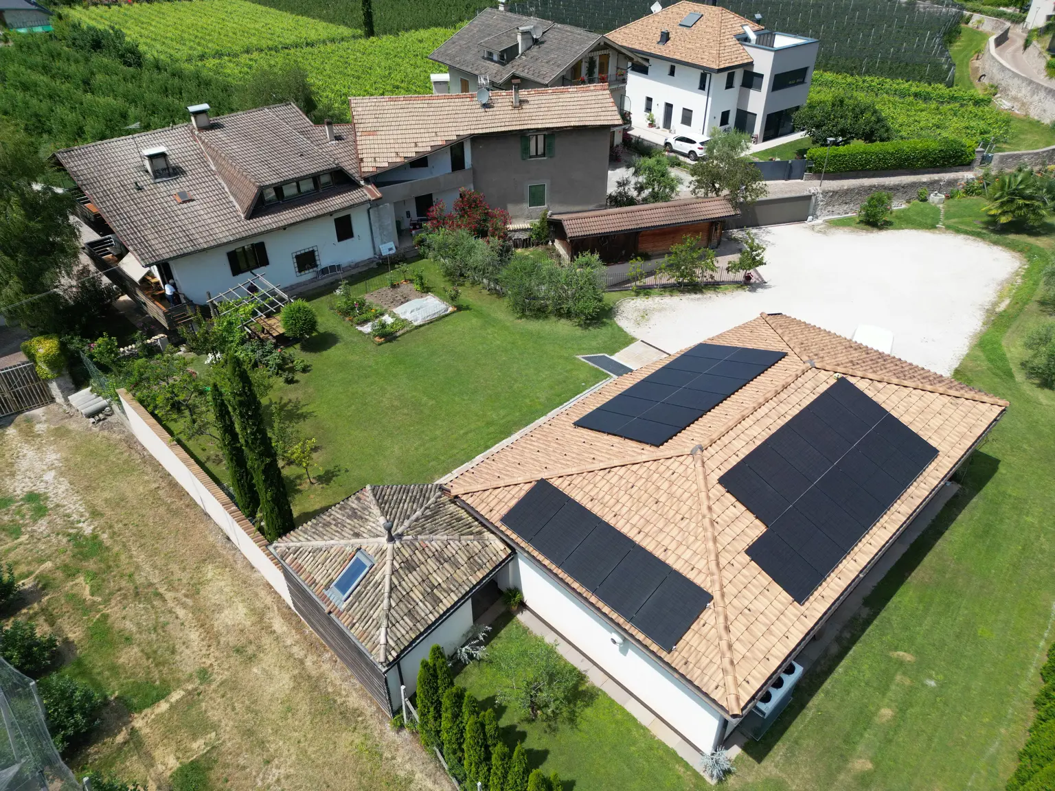 Aerial view of houses with solar panels on roofs, surrounded by greenery and small yards with driveways in a neighborhood.