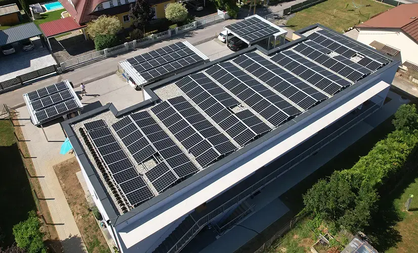 Multi-family house with rooftop PV panels; parking area in front has carports with PV panels on their roofs.