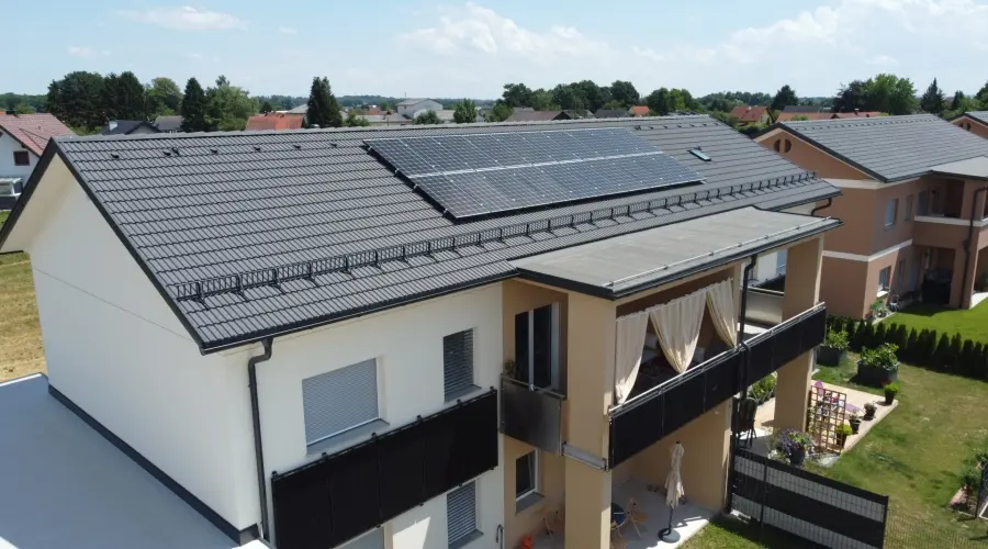 Four-unit house with rooftop PV panels, garden, and parking spaces; a my-PV car is in the foreground.