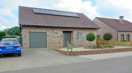 House with brick facade, stone garden, and two small trees in the front yard; on the roof are PV panels.