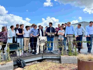 A group of people standing on a rooftop deck, some holding an object, with a cloudy sky in the background.