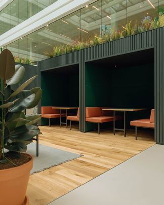 Modern indoor seating alcoves with wooden floors, green walls, and orange benches, surrounded by glass and plants for a natural ambiance.