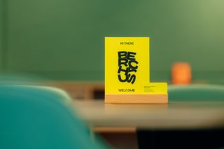 Yellow sign on a table in a green room reads "Hi there, because welcome" with a small card nearby.