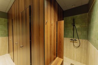 Locker room with wooden lockers and a shower area having green tiles and a black handheld showerhead.