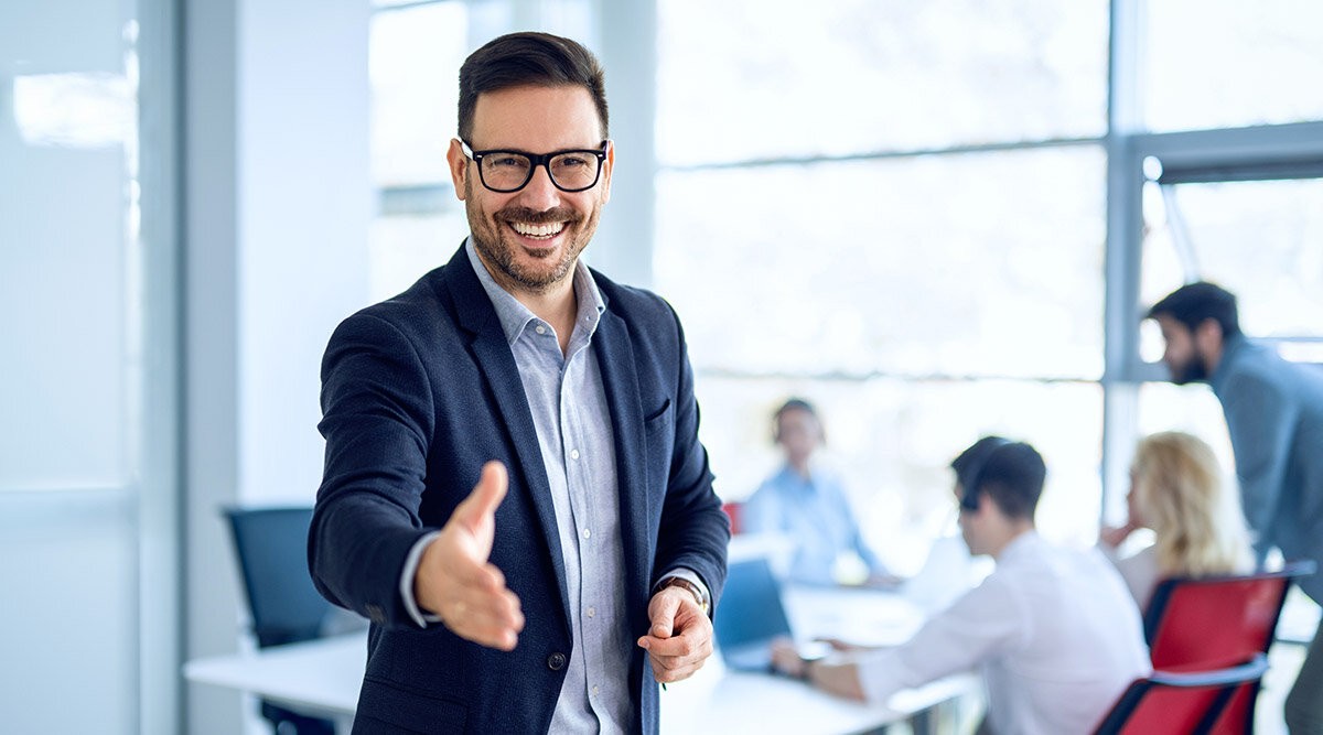 Um homem de terno e óculos está sorrindo e dando um polegar para cima em um ambiente de escritório.