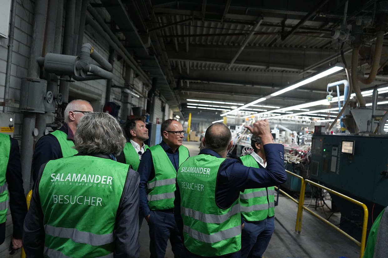 Um grupo de pessoas vestindo coletes verdes com as palavras "Salamander Besucher" neles estão em pé em uma fábrica.