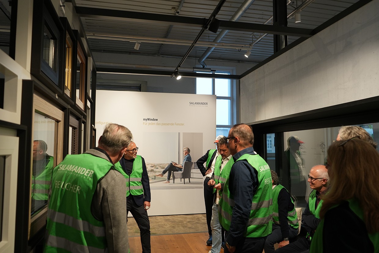 A group of people wearing green vests are gathered in a room with a large poster on the wall.