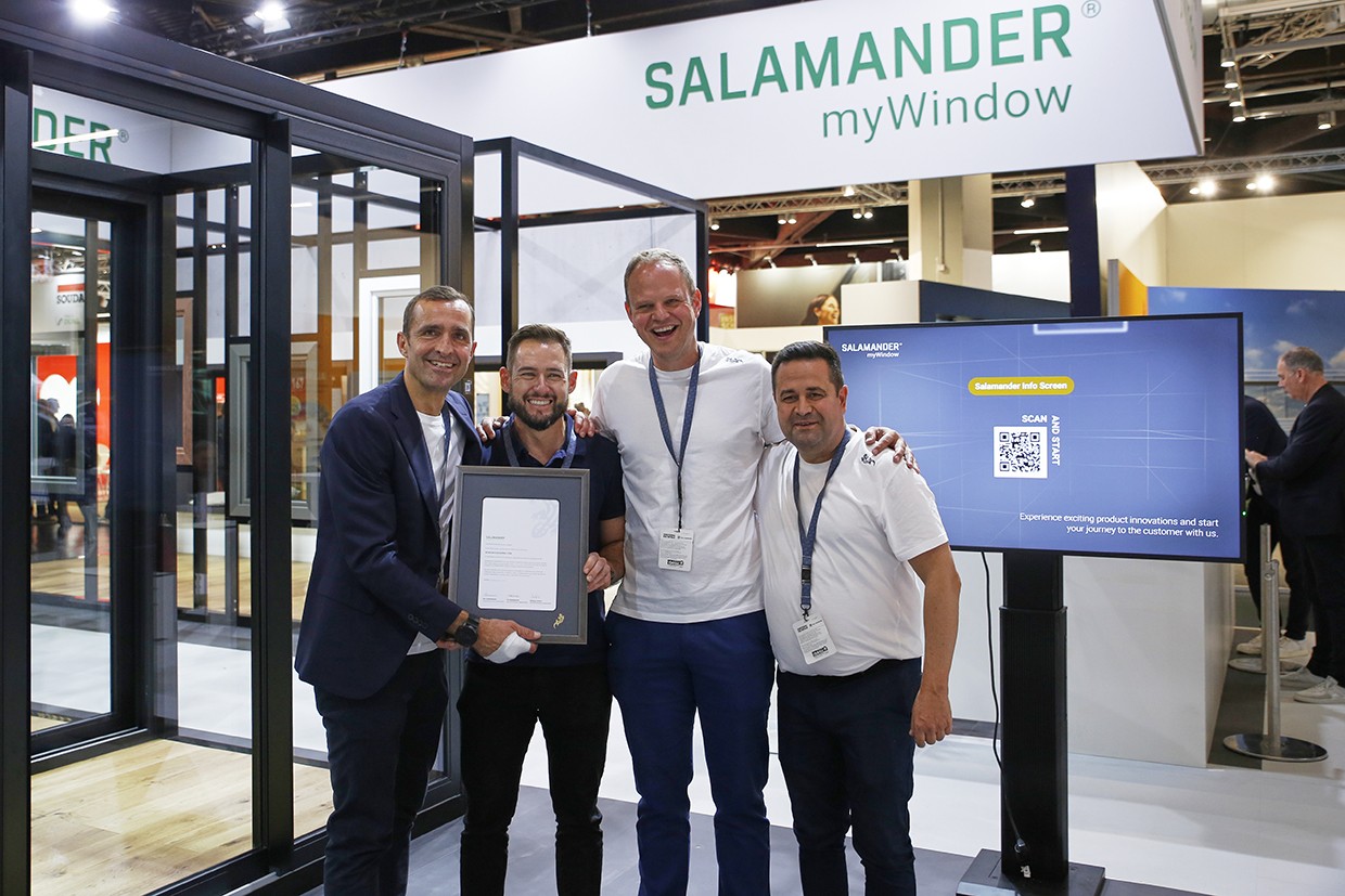 Four men stand together, smiling, in front of a Salamander myWindow display. The man on the left holds a framed certificate.