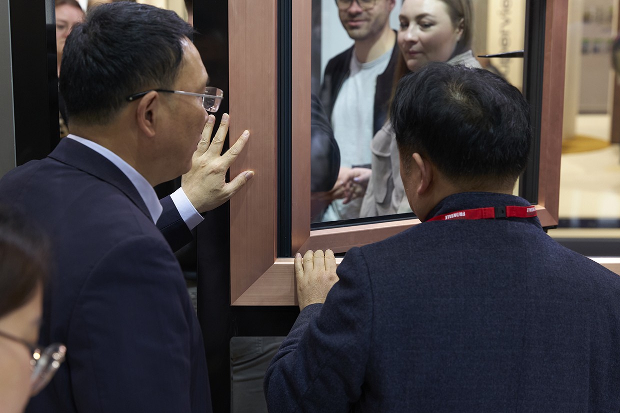Two men in suits are looking at a mirror with a reflection of a man and a woman.