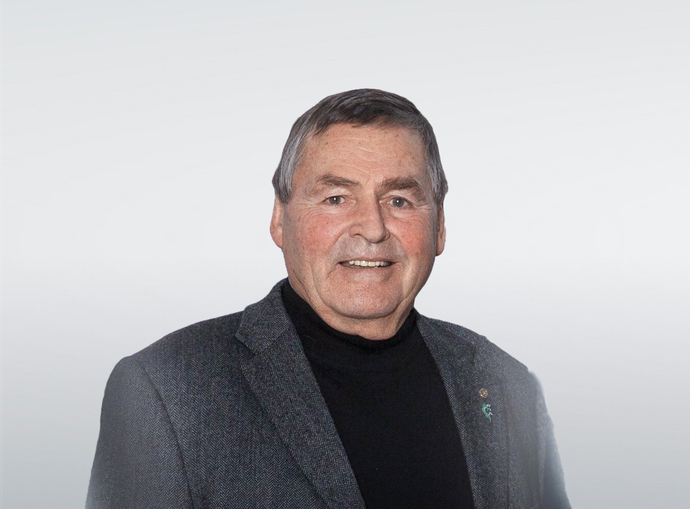 Portret van een lachende man in een grijze blazer en zwart coltrui tegen een witte achtergrond.