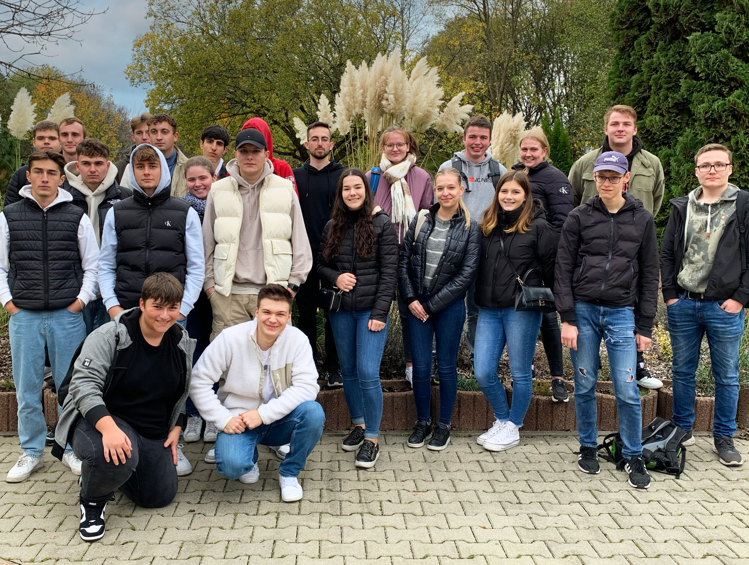 Um grupo de jovens está em pé e sentado em um parque, sorrindo e posando para uma foto.