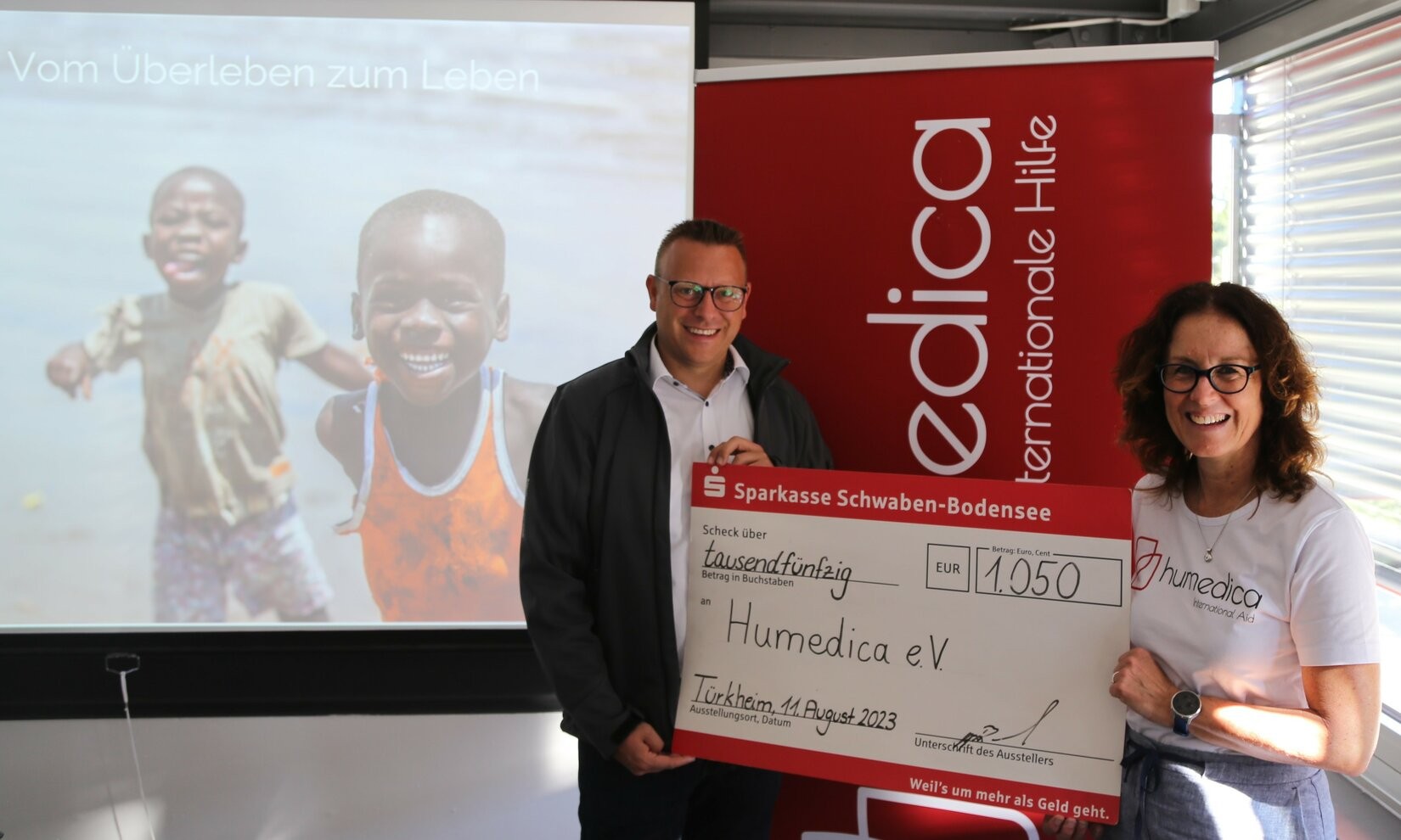 Two people holding a large check in front of a red banner with the word "edica" on it.