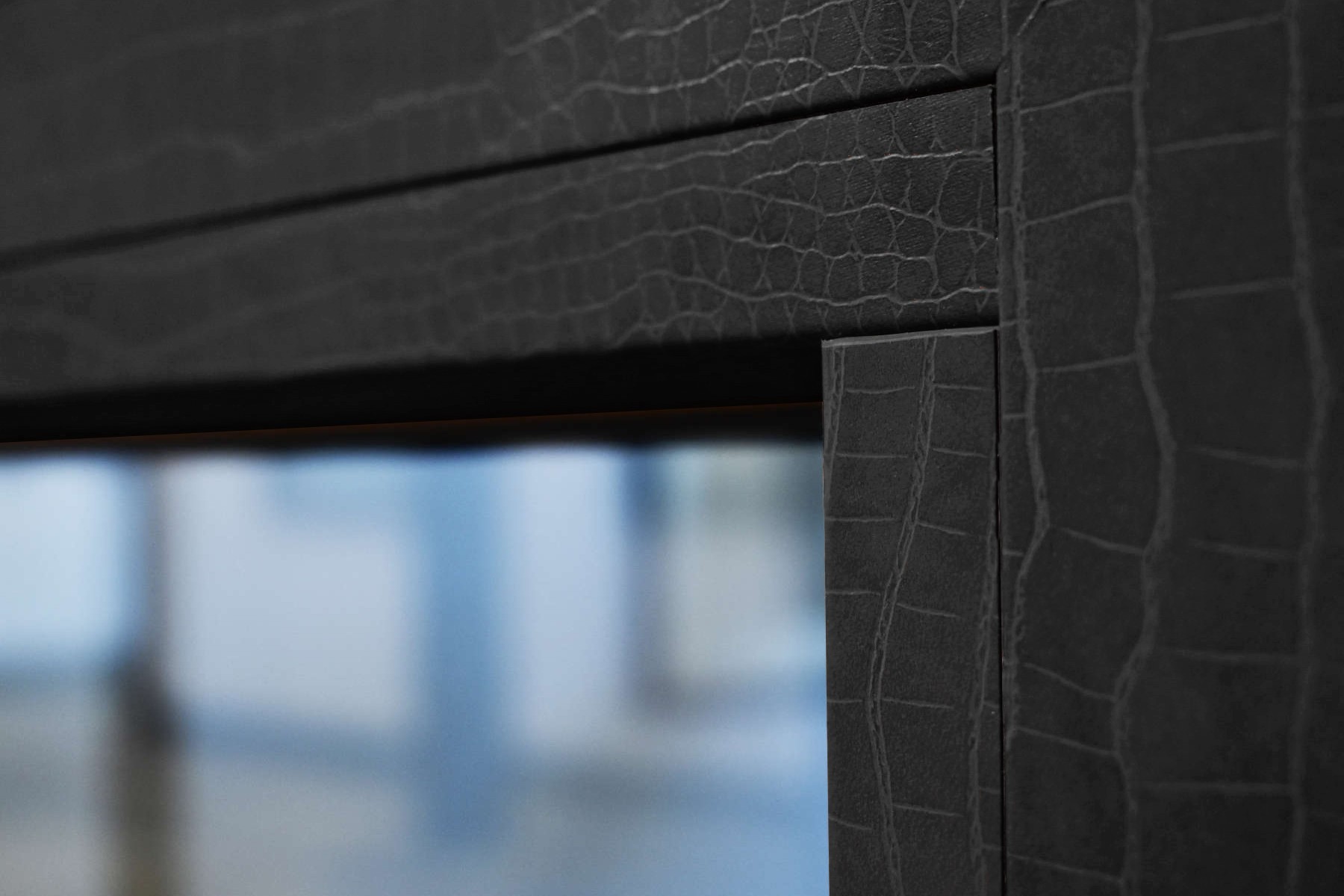 Primer plano de un marco de textura de cuero negro con una vista borrosa de una ventana de vidrio y un edificio en el fondo.