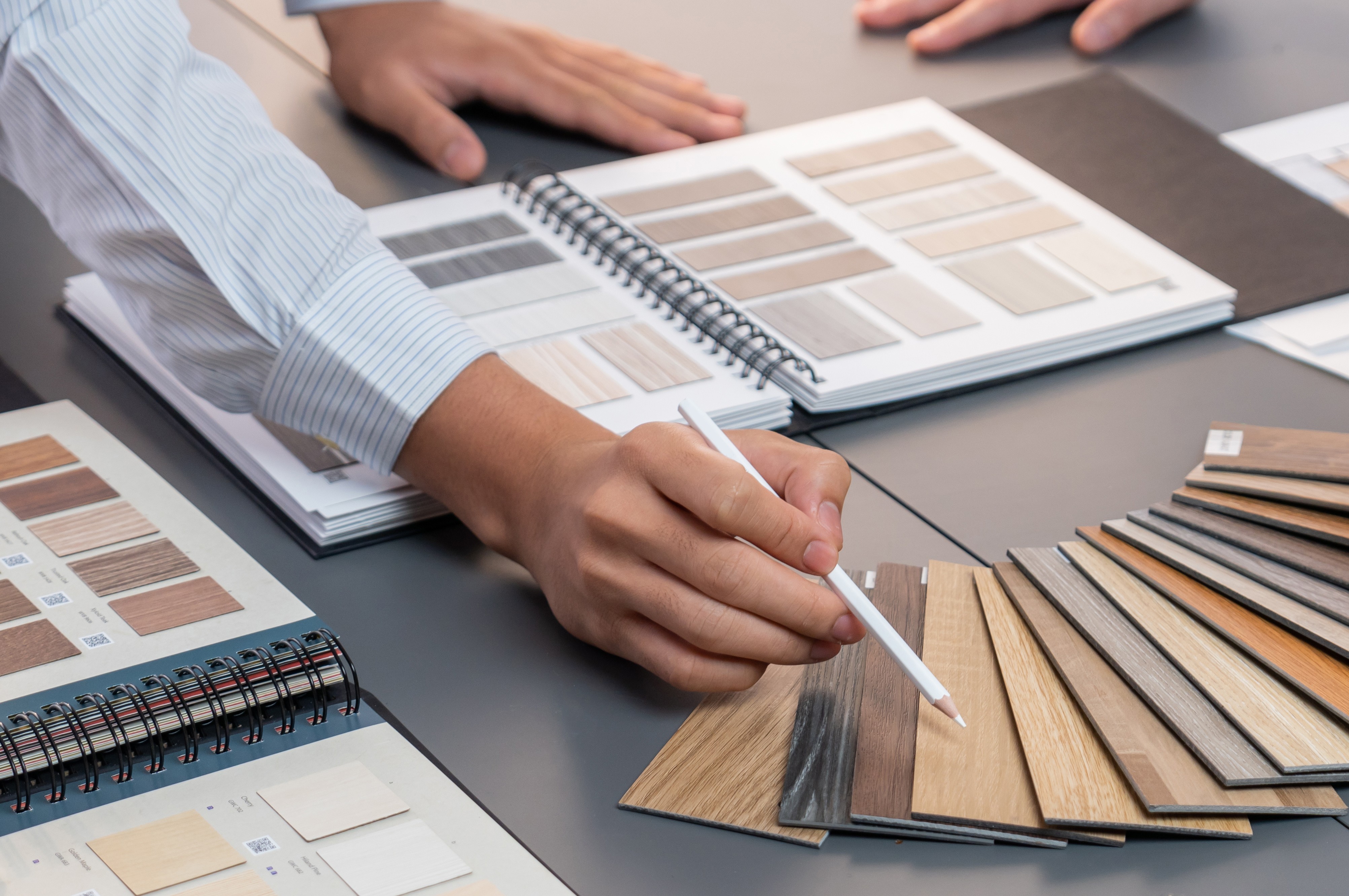 Una persona sta tenendo una matita e guardando una tavolozza di colori di campioni di legno su un tavolo.