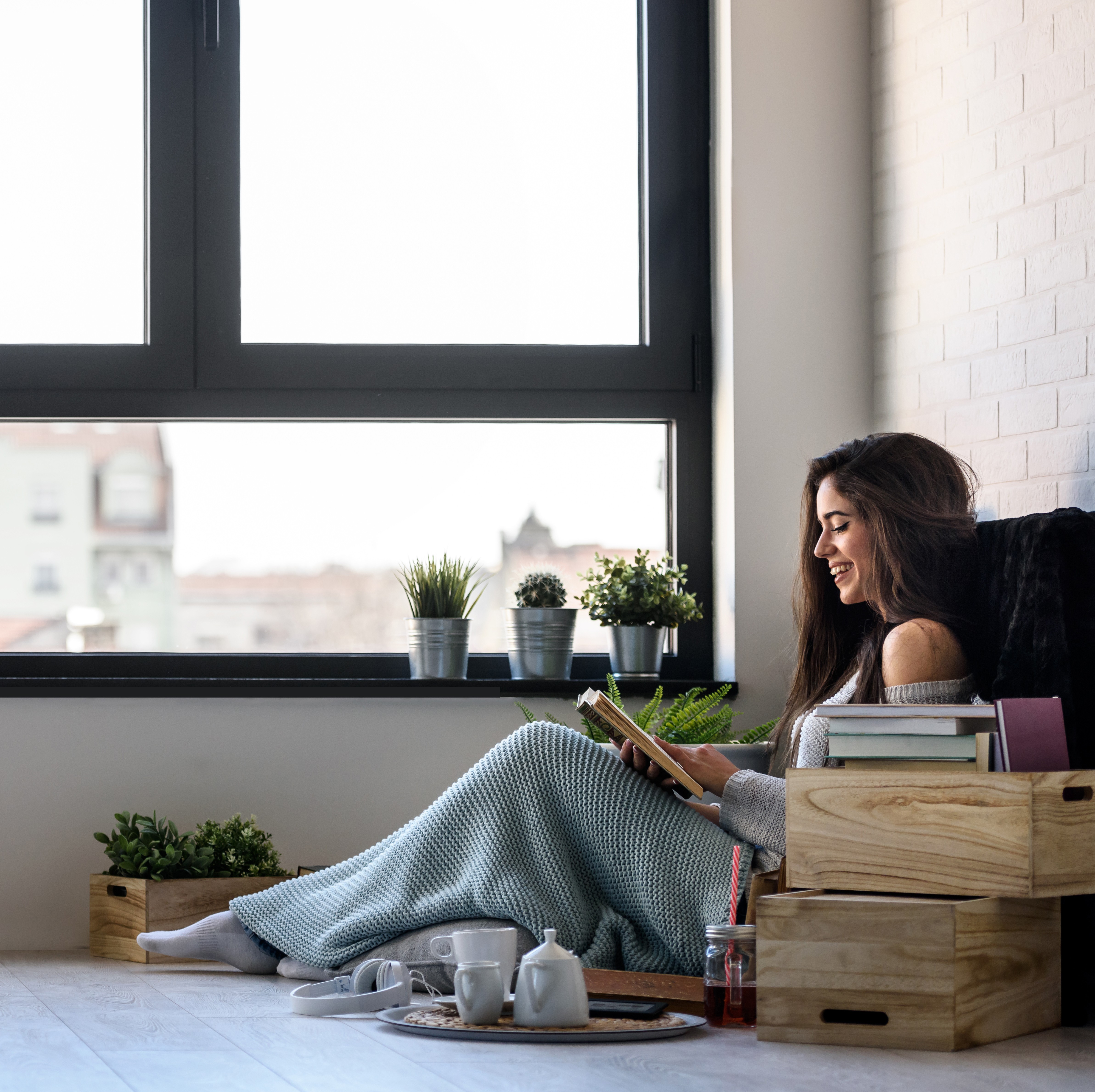 Donna seduta sul pavimento che legge un libro con una tazza di tè e un piatto di biscotti.
