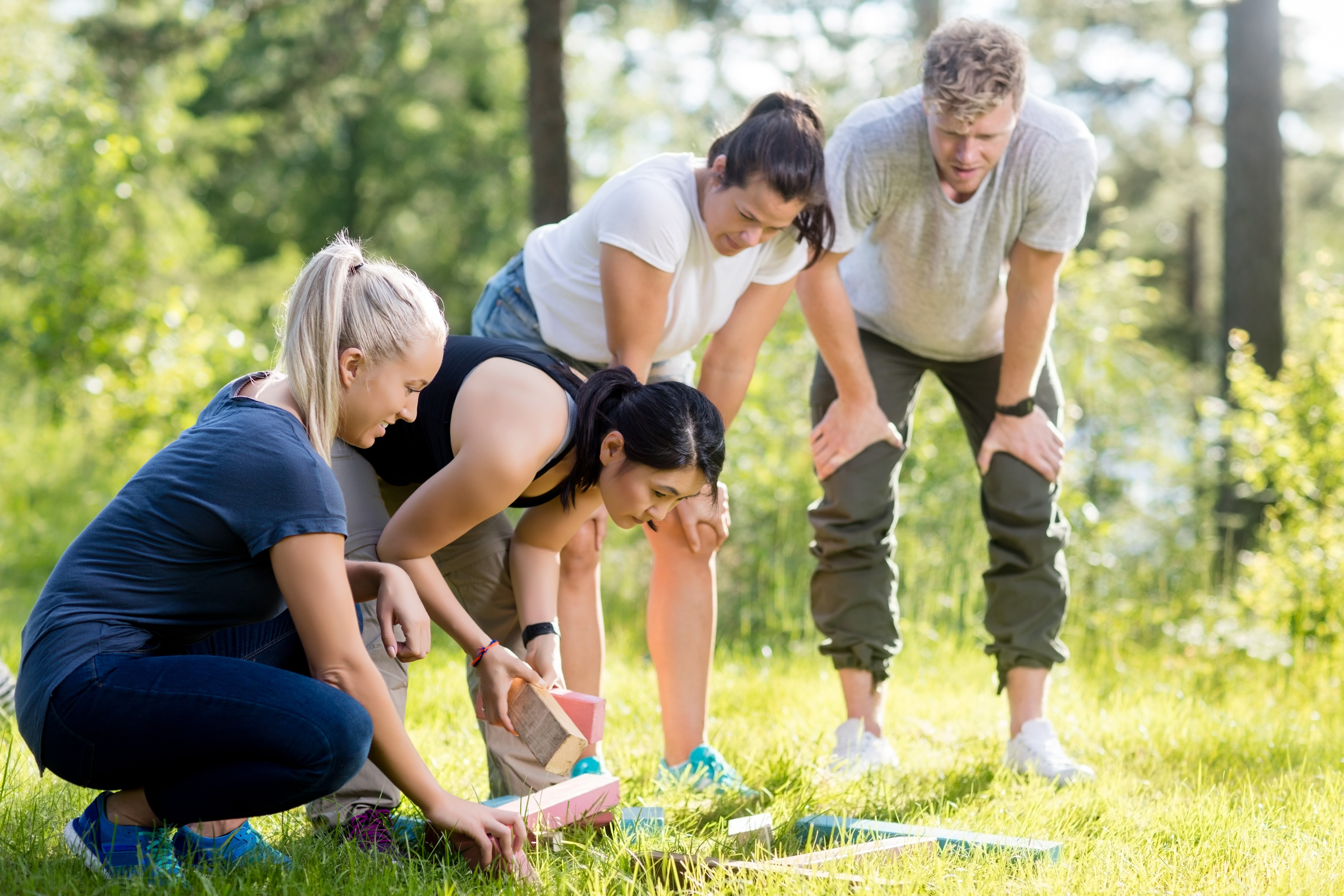 Cuatro personas están en un bosque y se están inclinando para recoger bloques de madera del suelo.