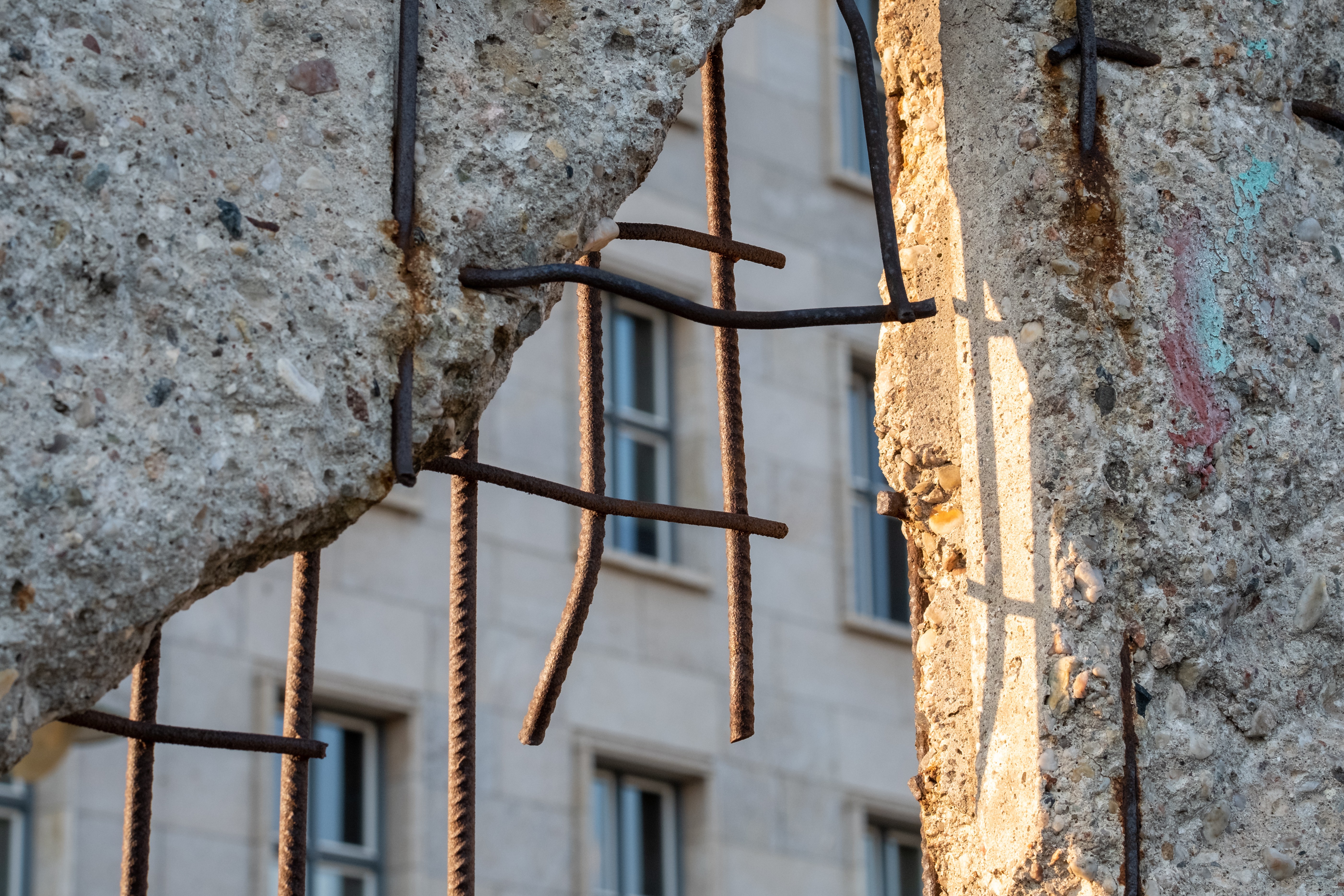 A close-up view of a concrete wall with rusty metal bars and a building in the background.