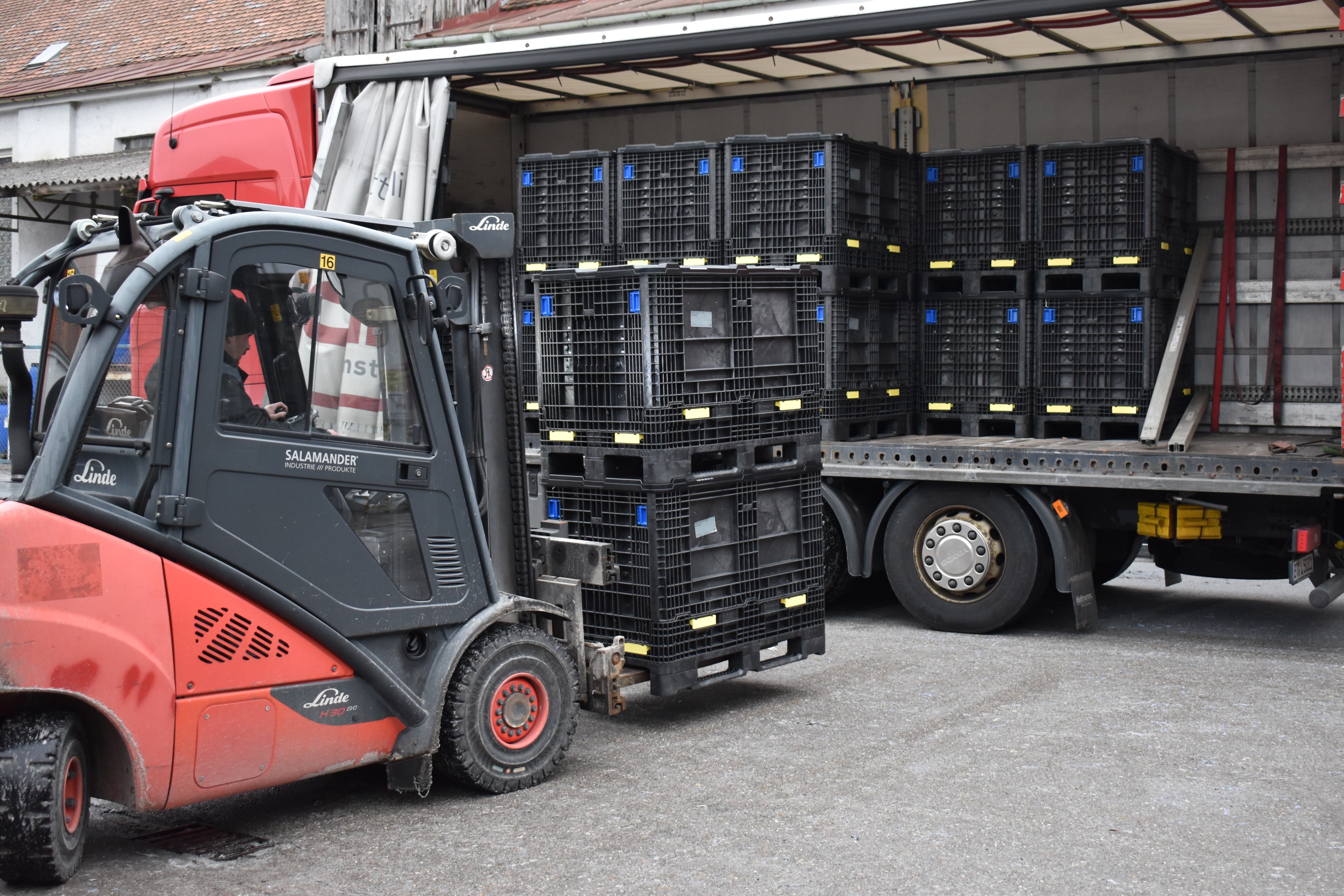A Linde forklift is parked next to a truck loaded with black crates, ready for unloading.