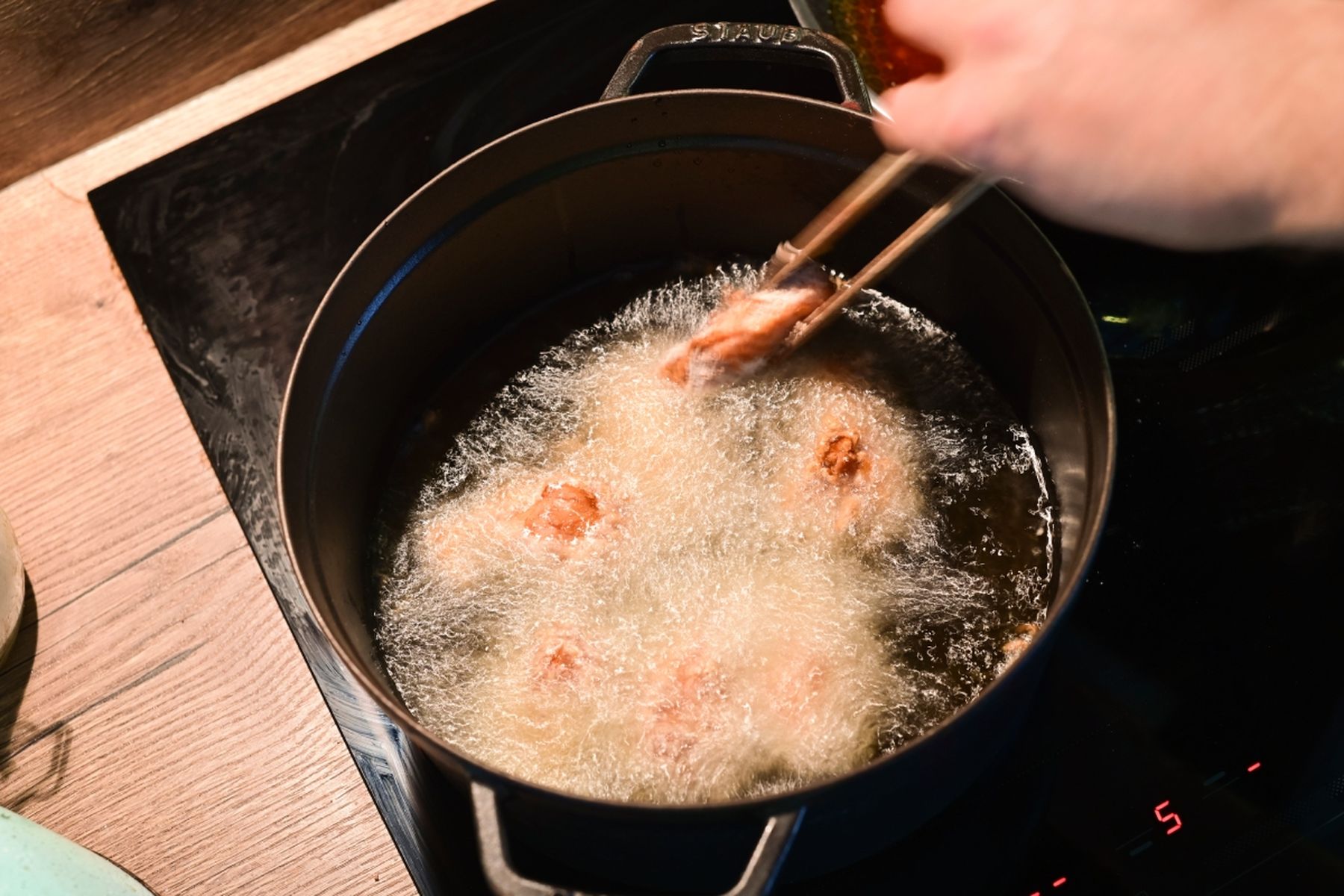 Kousky kuřete smažené v horkém oleji v hrnci na sporáku, ruka je obrací. Recept připravil Vojta Poštulka.
