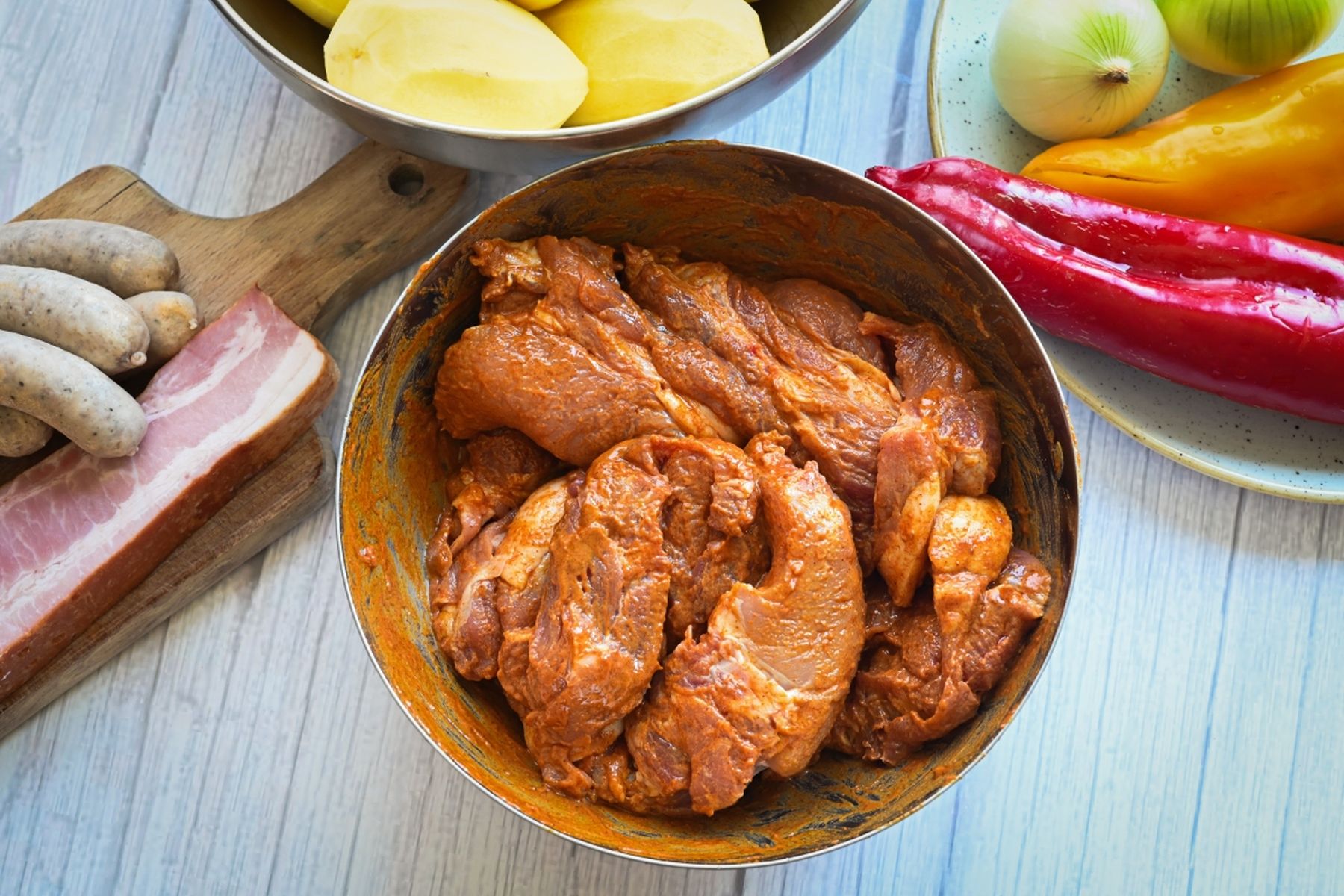 Naložené maso, klobásy a slanina na prkénku, vedle oloupané brambory, cibule a papriky v miskách na dřevěném povrchu. Recept připravil Vojta Poštulka.Naložené maso, klobásy a slanina na prkénku, vedle oloupané brambory, cibule a papriky v miskách na dřevěném povrchu. Recept připravil Vojta Poštulka.