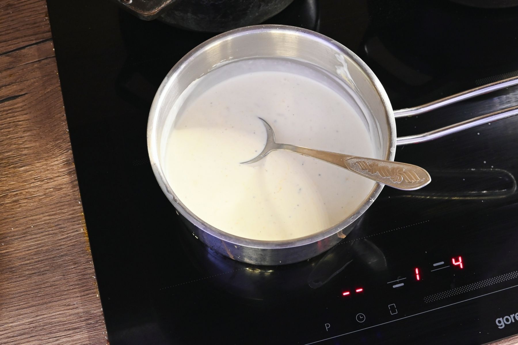 Hrnec se smetanovou směsí a lžící na elektrické varné desce.