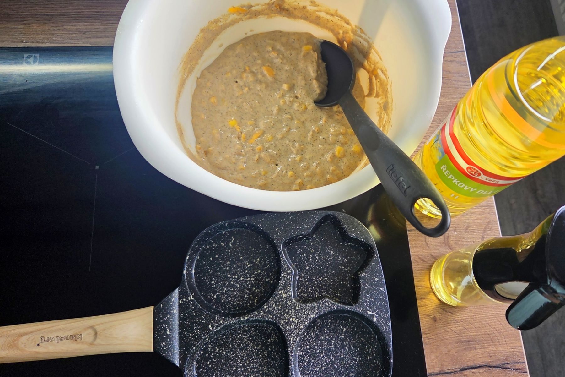 Těsto v bílé míse s naběračkou, pánev s formou na různé tvary lívanců a láhev řepkového oleje Váš Výběr na varné desce. Recept připravily Ségry v kuchyni.