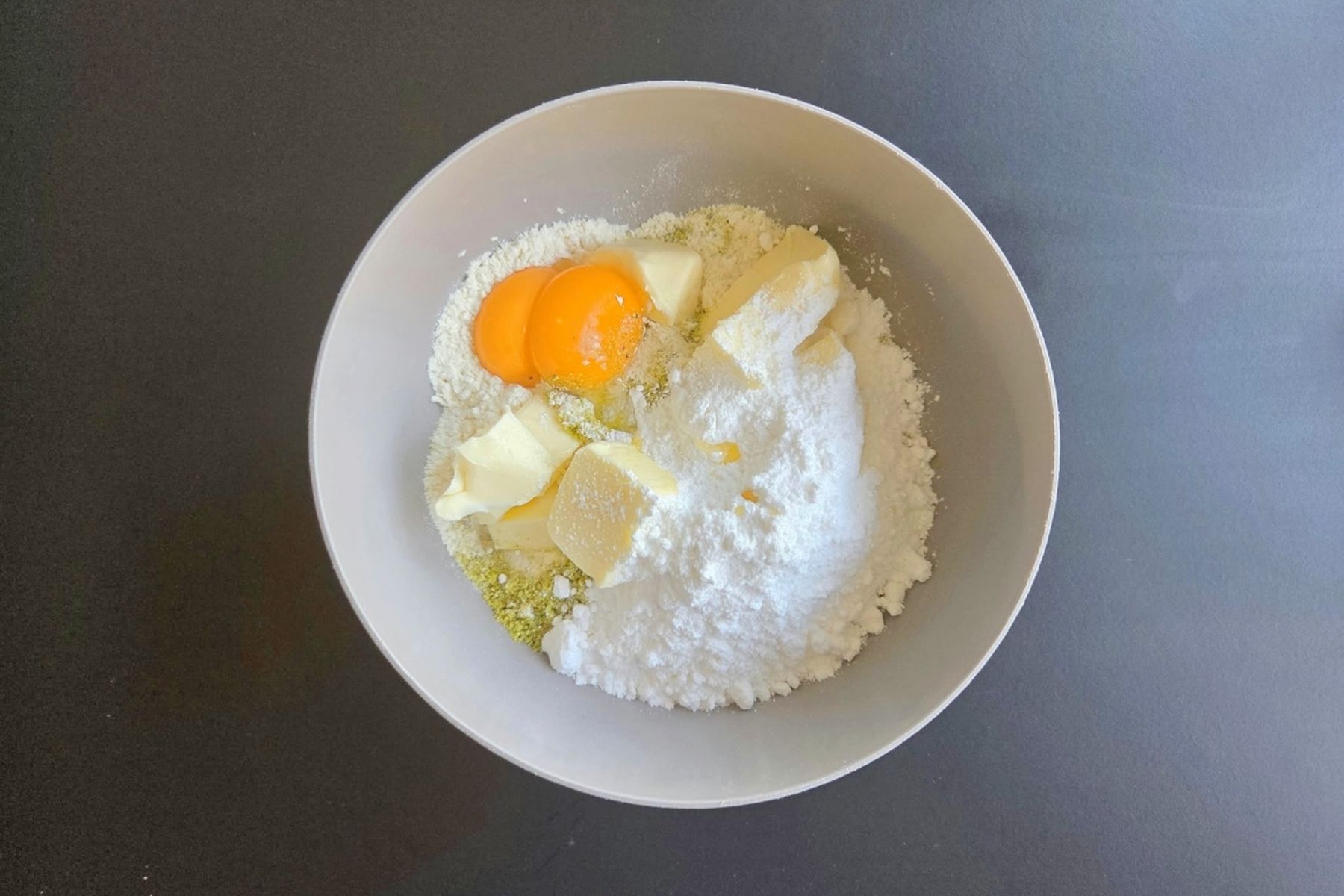 Mísa s moukou, cukrem, kousky másla a dvěma žloutky na tmavé pracovní ploše, připravené na přípravu těsta. Recept připravily Ségry v kuchyni.
