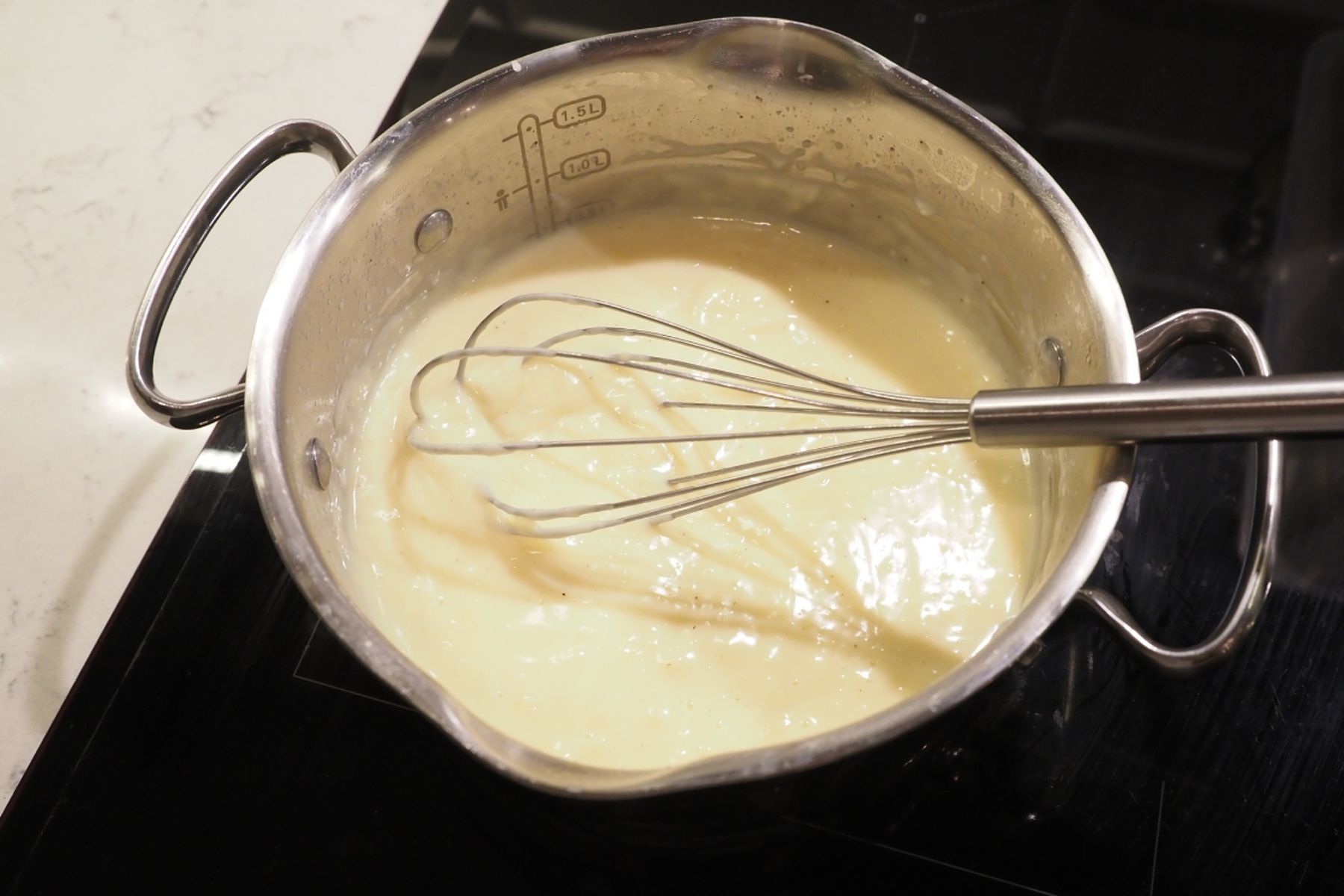 Nerezový rendlík s metličkou, ve kterém se na černé varné desce míchá puding.