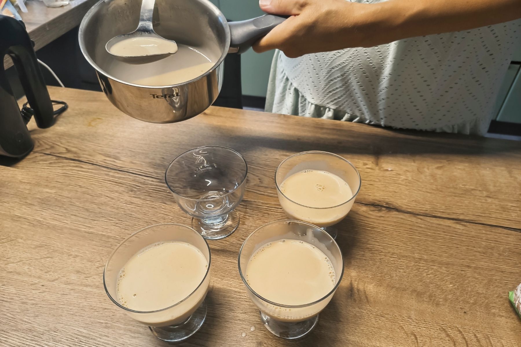 Osoba nalévá krémovou směs z hrnce do tří skleniček na dřevěném stole, vedle stojí prázdná sklenička. Recept připravily Ségry v kuchyni.
