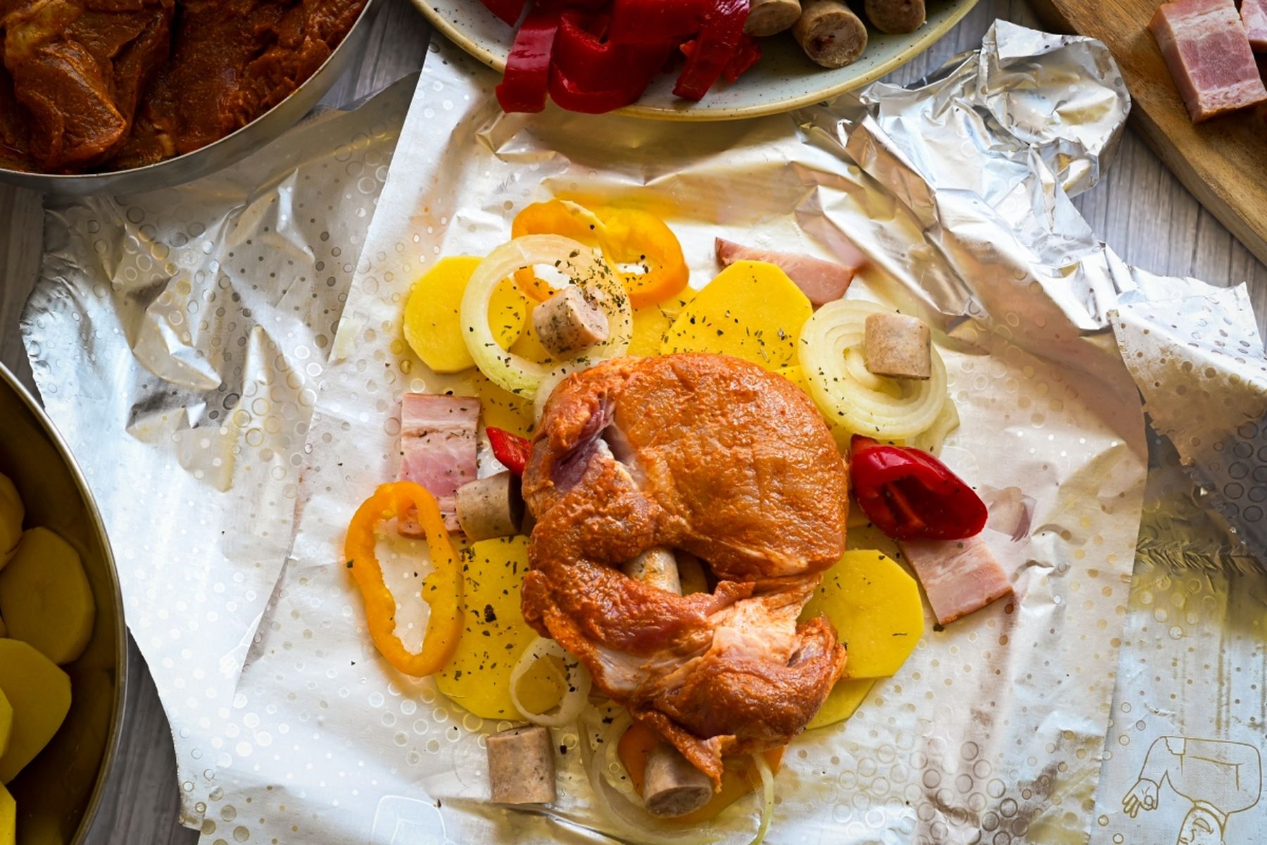 Ochucená krkovice s nakrájenými bramborami, cibulí a paprikou na alobalu, připravená k pečení. Recept připravil Vojta Poštulka.
