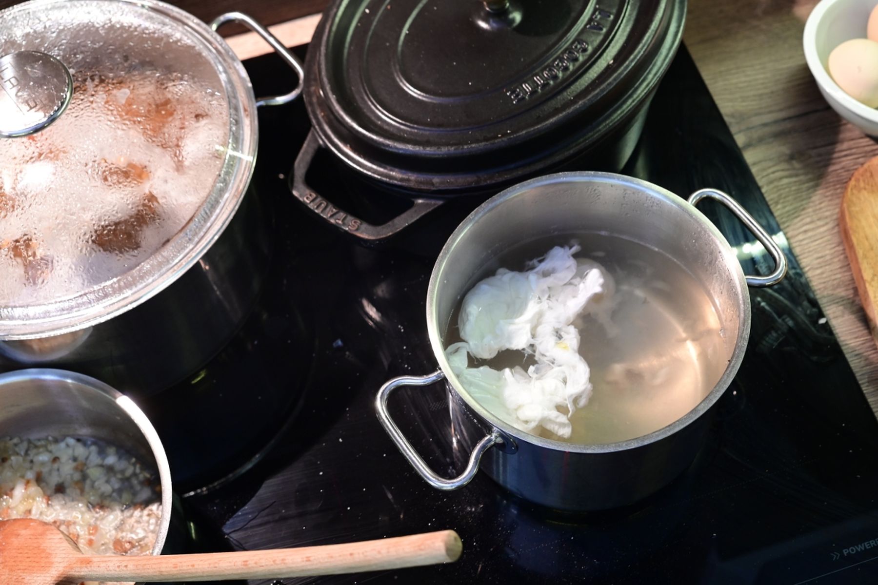 Varná deska s několika hrnci – v jednom se ve vodě pošírují dvě vejce, v druhém se restují cibulky s dřevěnou vařečkou. Jedná se o recept z nabídky Globus.