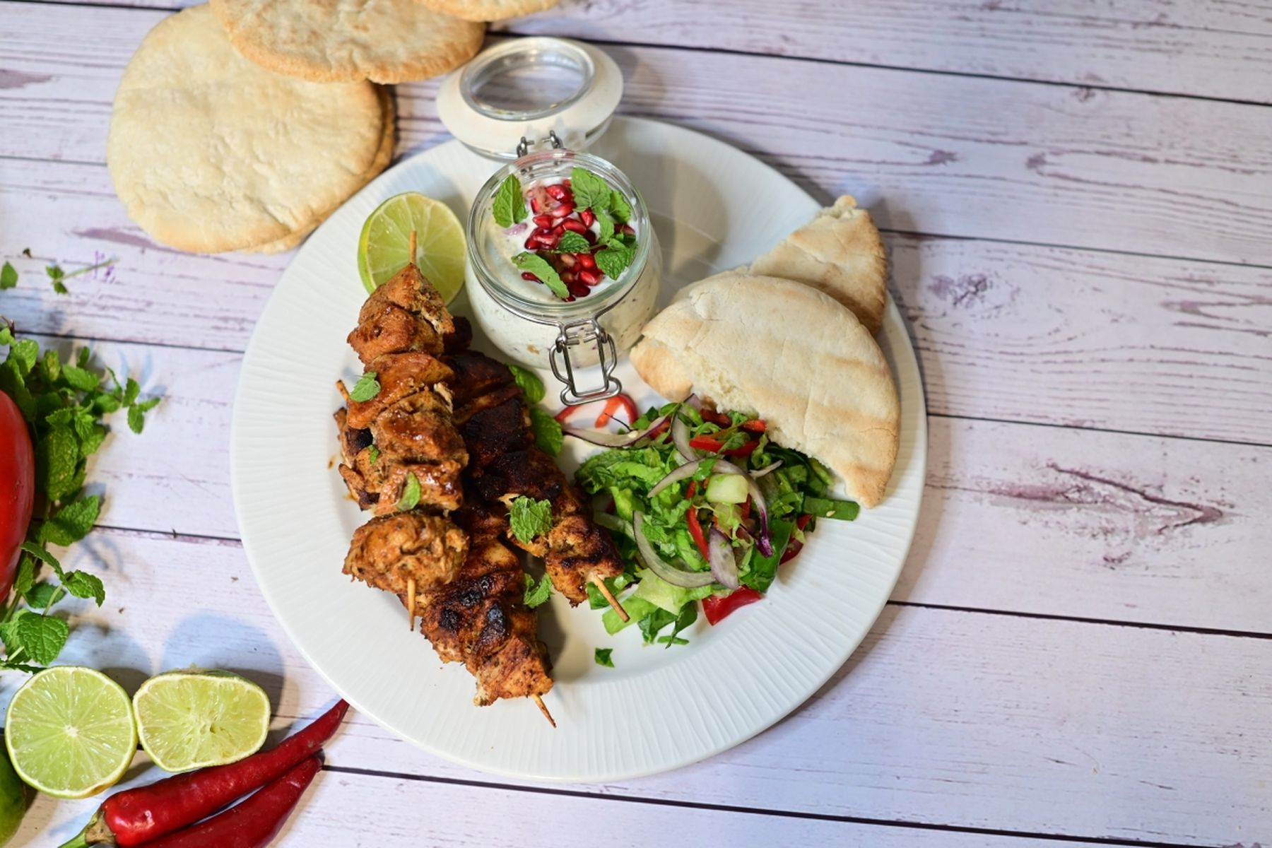 Talíř s kuřecím kebabem, pita chlebem a salátem, ozdobený limetkou a bylinkami na dřevěném stole, podle receptu na kuřecí kebab z hypermarketu Globus od Vojty Poštulky.