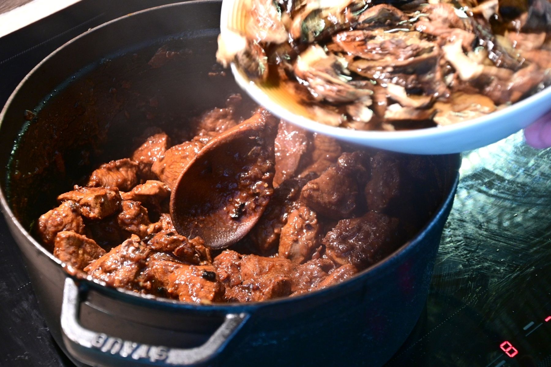 Hrnec s dušeným hovězím masem a dřevěnou vařečkou, do kterého se z misky přidávají houby. Recept připravil Vojta Poštulka.