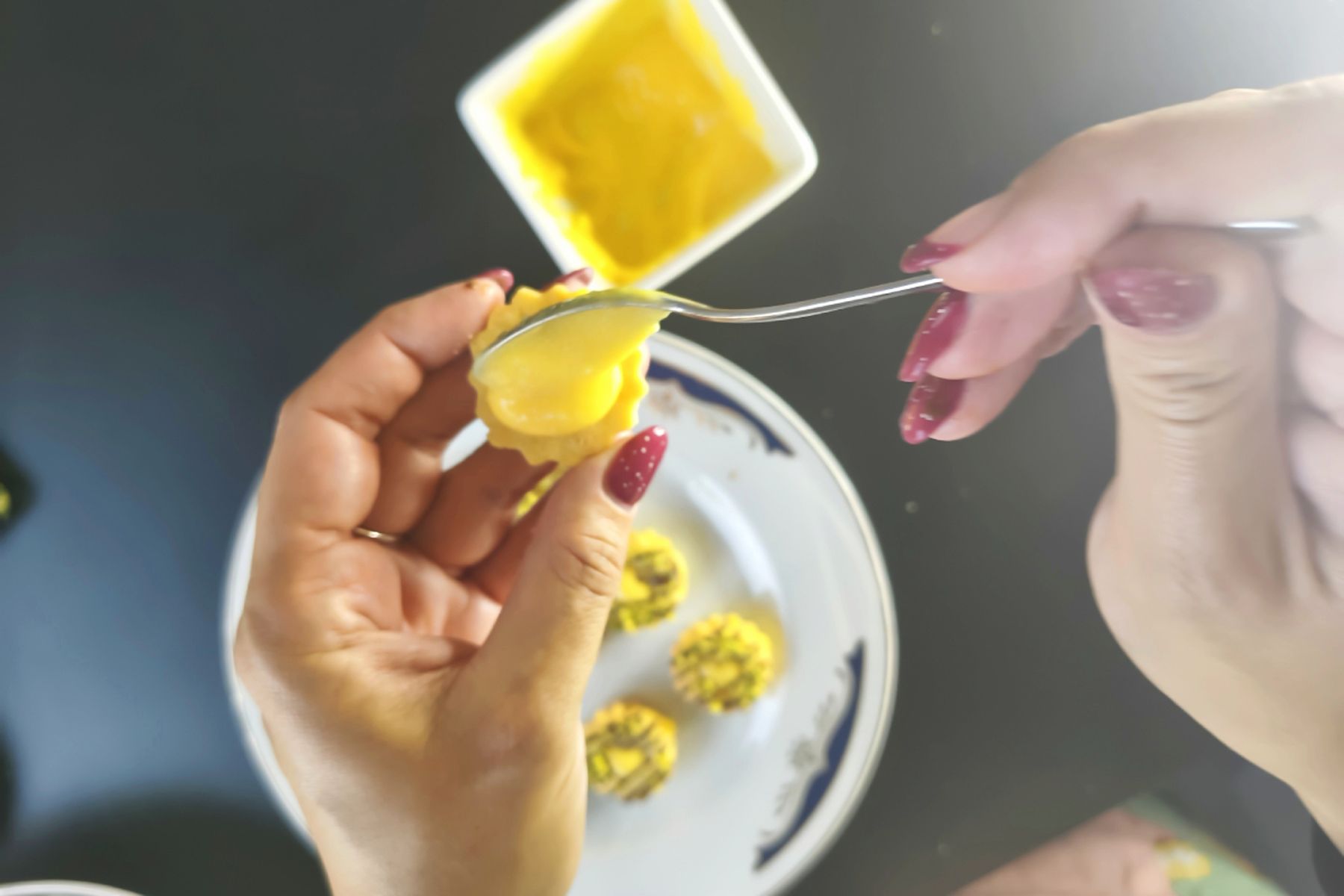 Ruka roztírá lžičkou pomerančový curd na linecké cukroví, v pozadí jsou vidět další kousky. Recept na tradiční linecké cukroví připravily Ségry v kuchyni.
