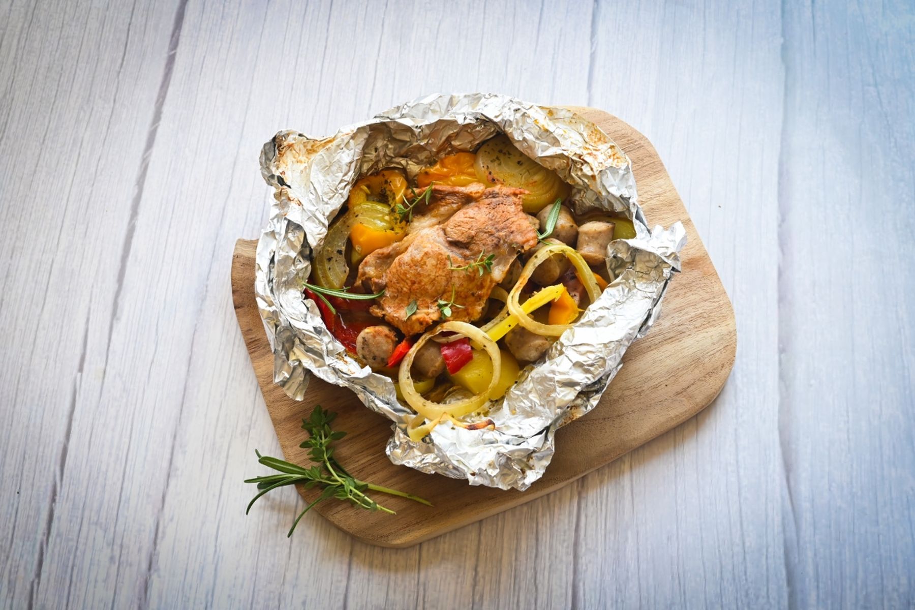 Pečená krkovice v alobalu s paprikou, cibulí a bylinkami na dřevěném prkénku. Recept připravil Vojta Poštulka.