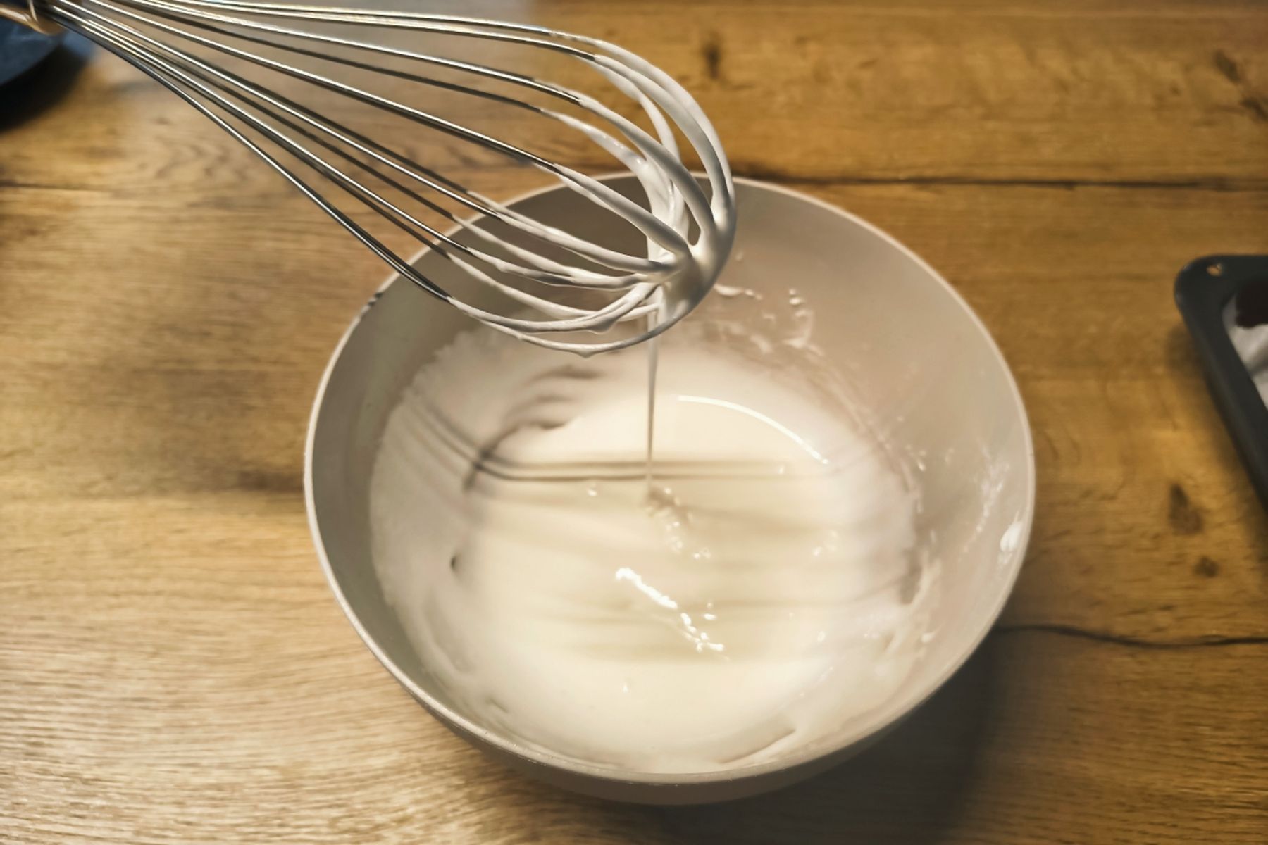 Kovová metlička nechává stékat bílou směs do mísy na dřevěné pracovní desce. Recept připravily Ségry v kuchyni.