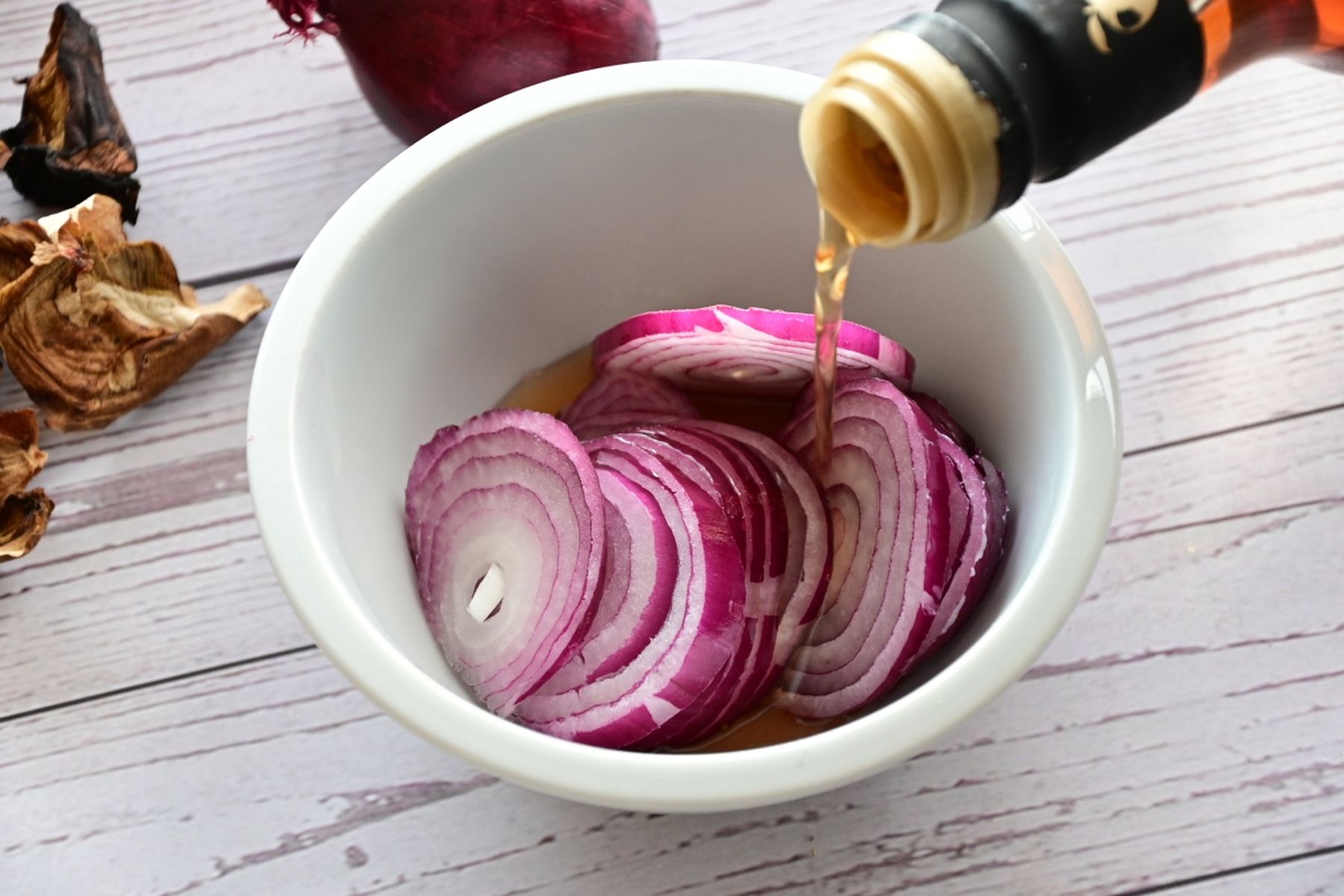 Nakrájená červená cibule v misce, do které se nalévá vinný ocet z láhve. Recept připravil Vojta Poštulka.