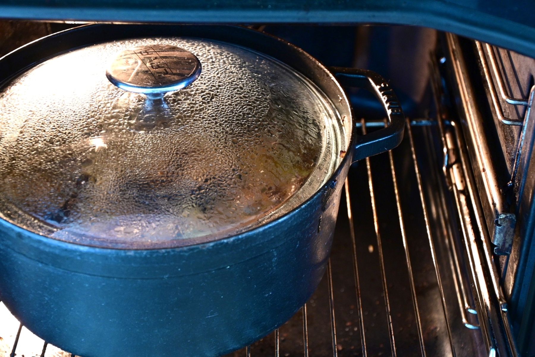 Černý hrnec se skleněnou poklicí pečící se v troubě, na poklici je vidět sražená pára. Recept připravil Vojta Poštulka.