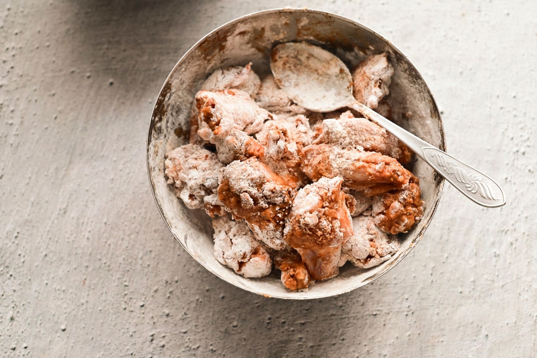 Miska se syrovými kuřecími křidélky obalenými v mouce, vedle leží lžíce, připraveno na smažení. Recept připravil Vojta Poštulka.