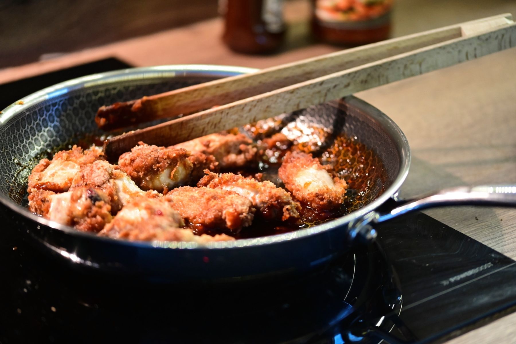 Smažené kousky kuřete na pánvi obracené dřevěnými kleštěmi na sporáku, v tlumeném osvětlení kuchyně. Recept připravil Vojta Poštulka.